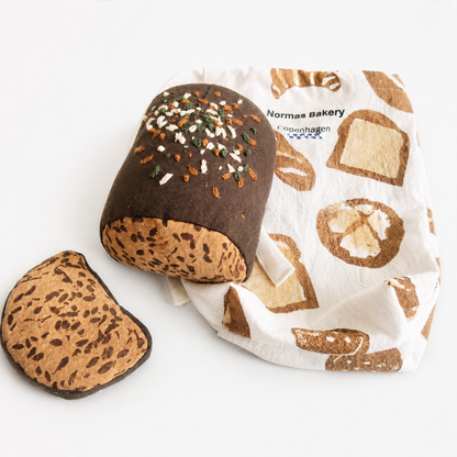 Handmade fabric rye bread loaf with one slice and a printed bakery cotton bag on a white studio background.