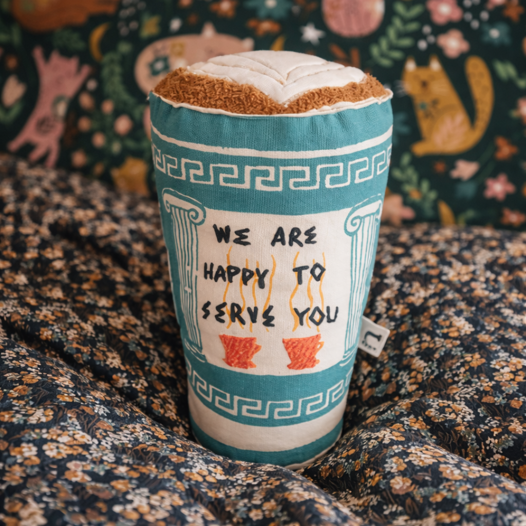 Textile item resembling a coffee cup with decorative design and text on a patterned fabric background