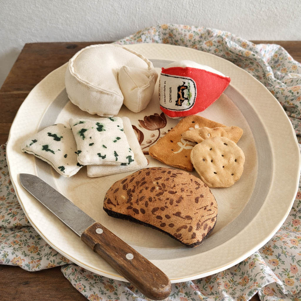 Handmade fabric lunch set with rye bread slice, cheese, crackers and small deli pieces on a plate with a wooden-handled knife.
