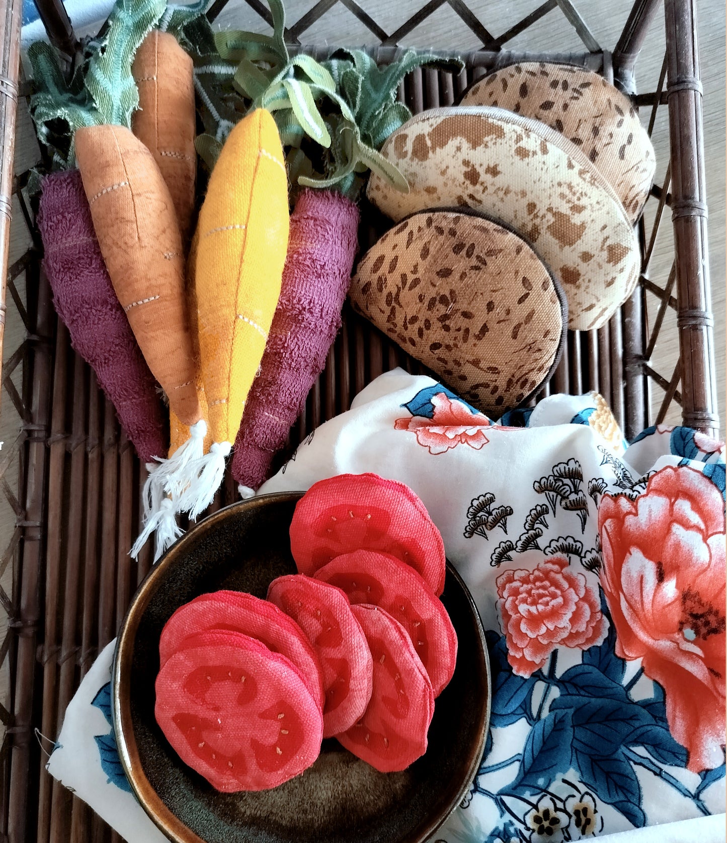 "A display of fabric play food in a wicker tray, including textile carrots, sourdough bread slices, seeded rolls, and tomato slices in a bowl, with a floral cloth."
"Et udvalg af legetøjsmad i stof i en fletbakke, herunder gulerødder i tekstil, surdejsbrødskiver, kernerundstykker og tomatskiver i en skål, med en blomstret klud."