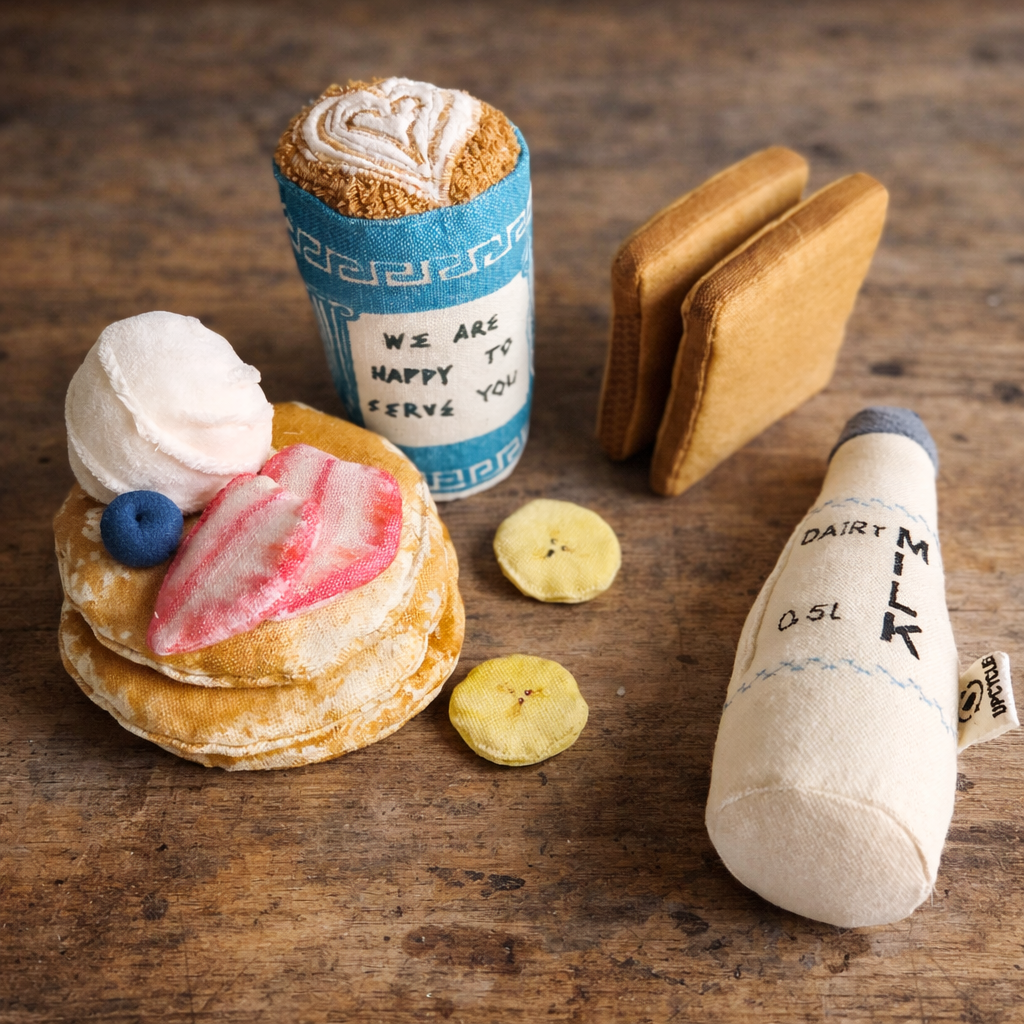 Toy food items including pancake, toasted bread, coffee cup and bottle on a wooden surface